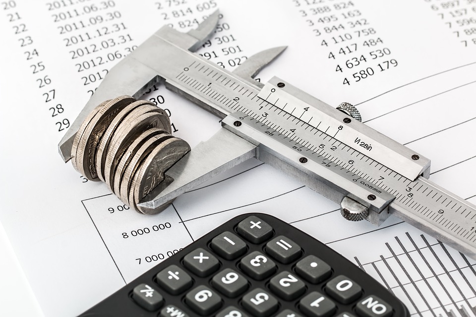 A stack of coins in a measuring device next to budget papers and a calculator